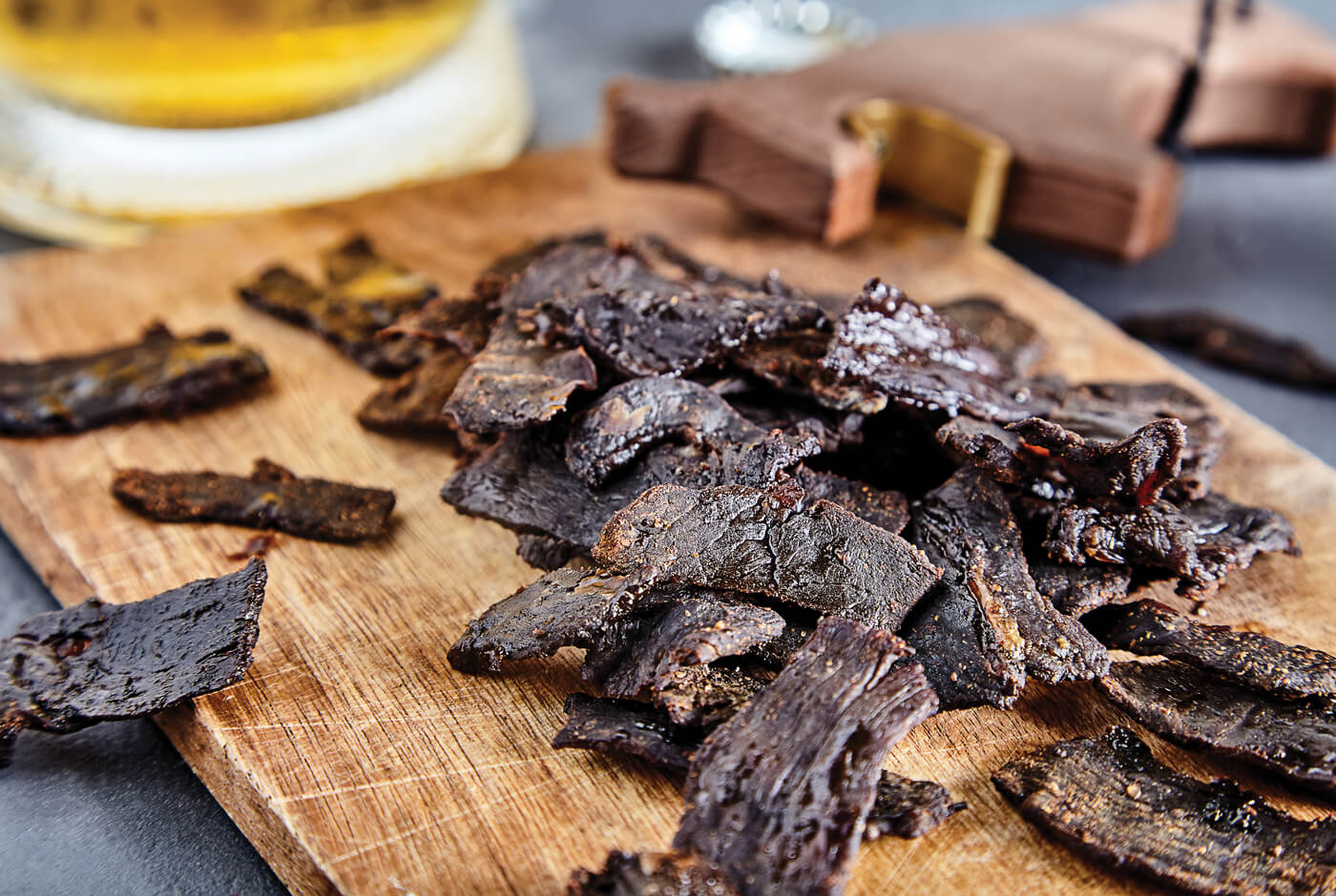 Darker brown strips of jerky arranged in a pile on a wooden cutting board.