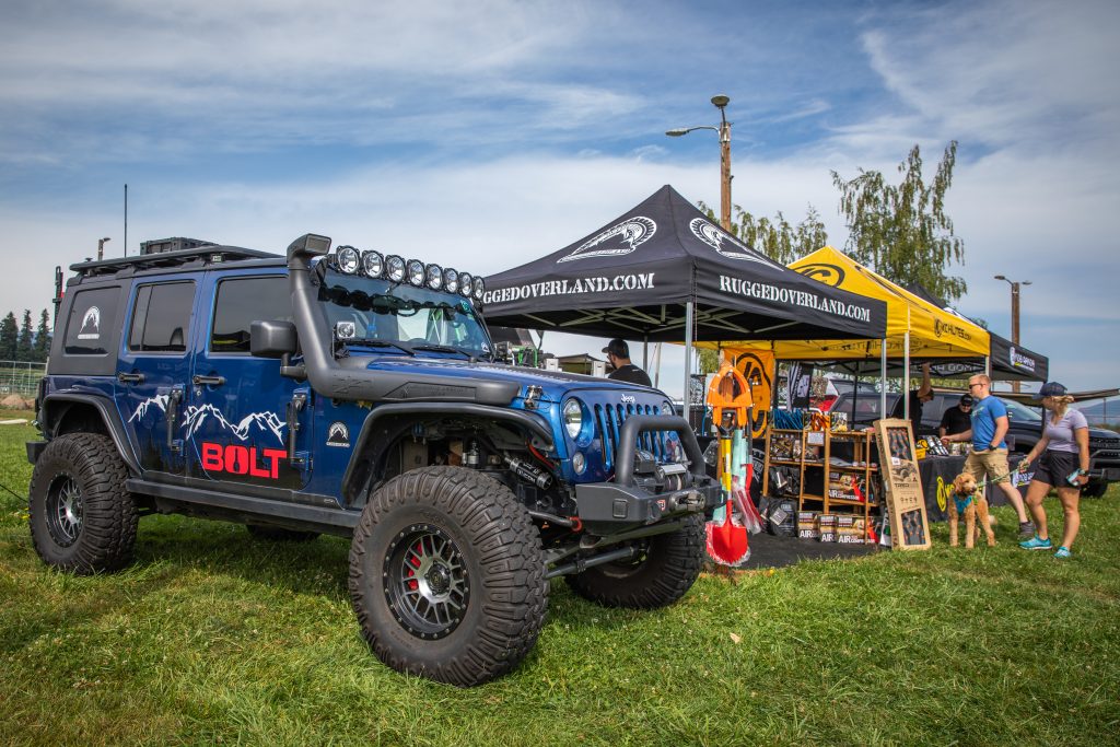 Toyo Tires Trailpass: Rugged Overland.com booth next to blue Jeep Wrangler