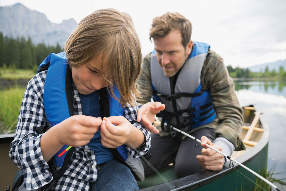 Boy ties a lure to a fishing line while father looks on to help.