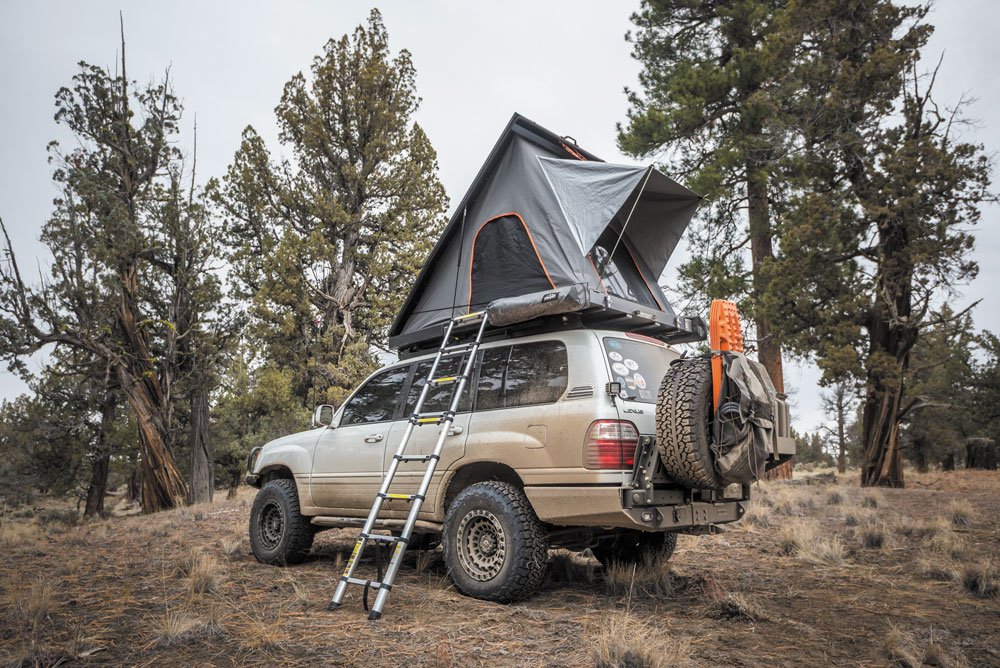 Lexus LX470 roof top tent parked in area with trees.