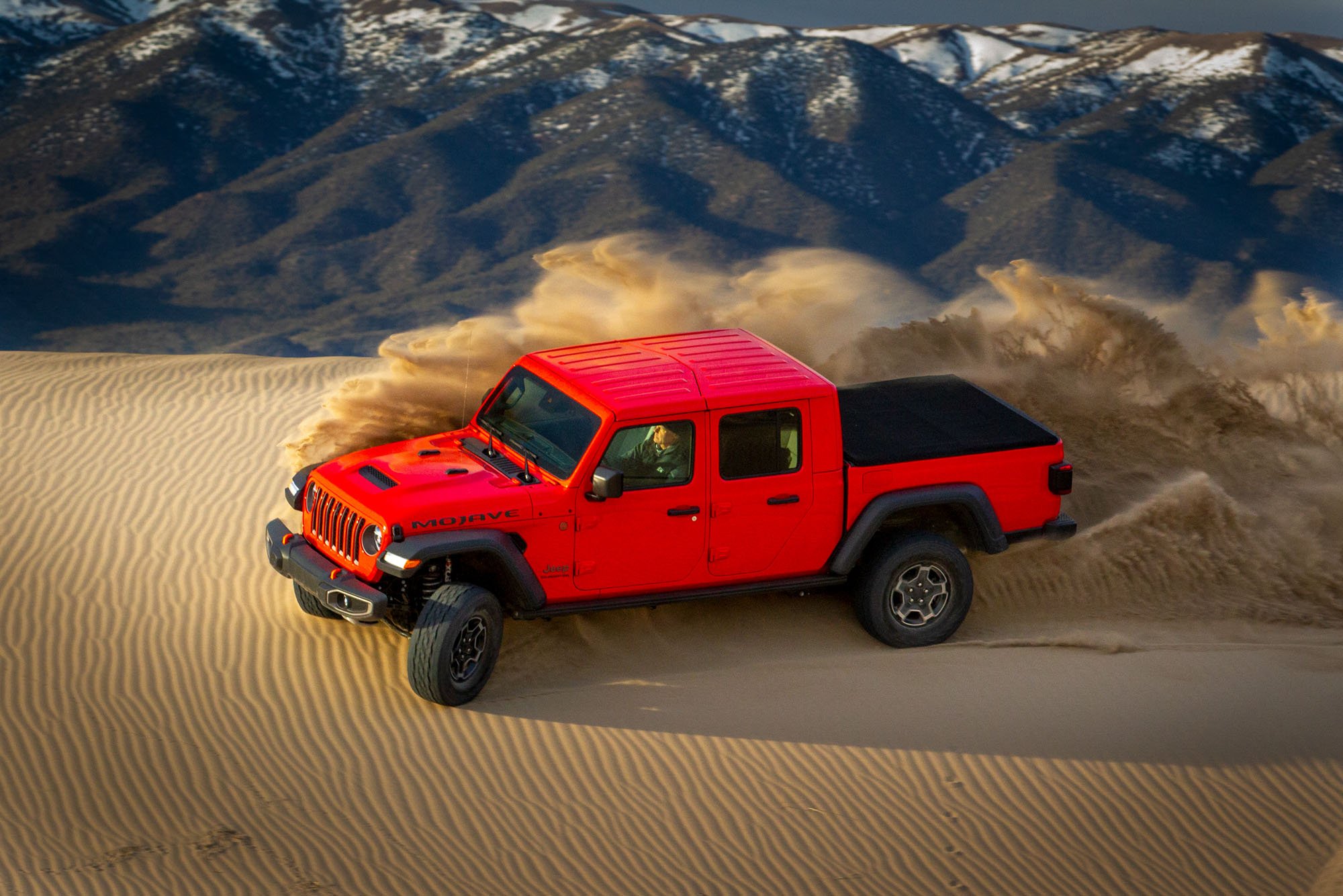 Red Jeep Gladiator turns up sand in desert.