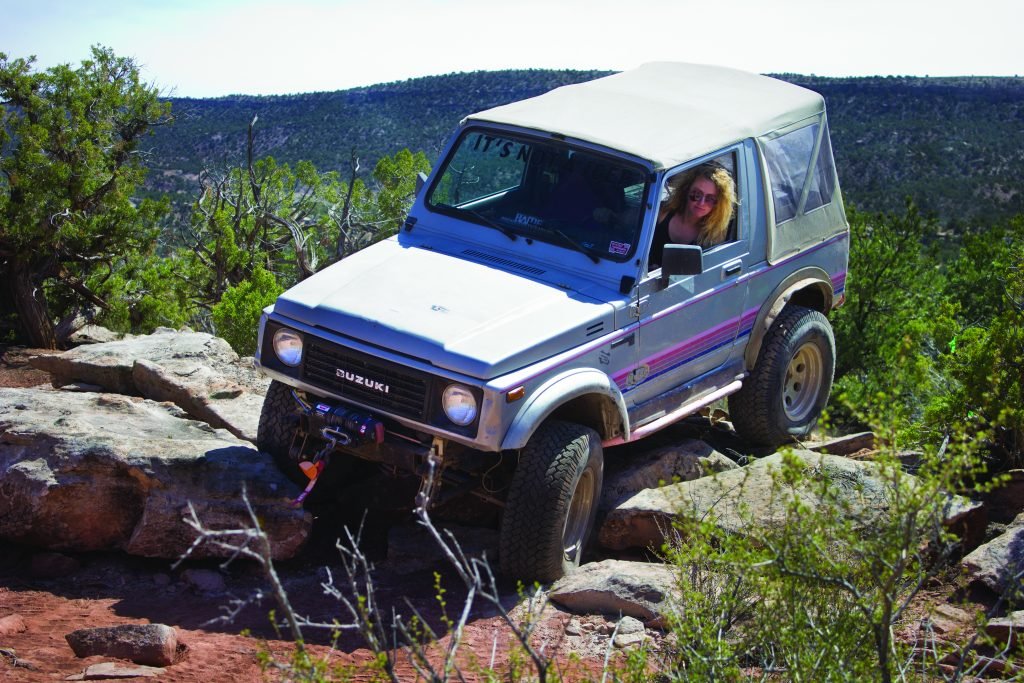 Women driving Suzuki Samurai over smooth rock ledges