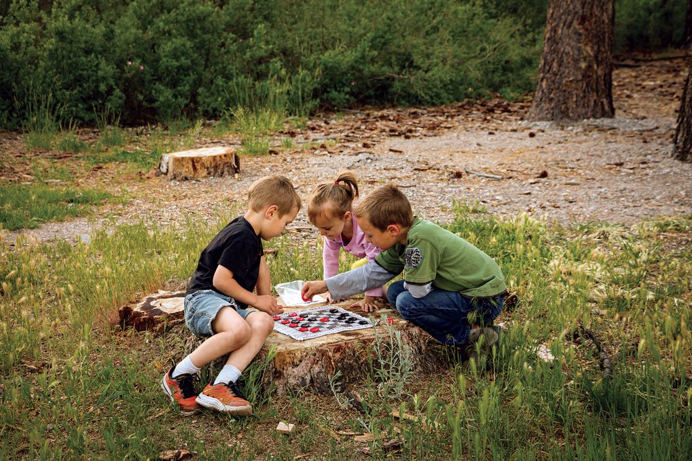 Three kids playing checkers using a log as a table