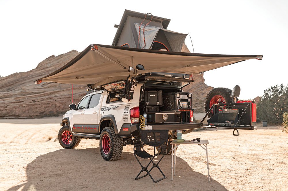 The white Tacoma truck parks in the desert with awning and fold-out kitchen deployed.