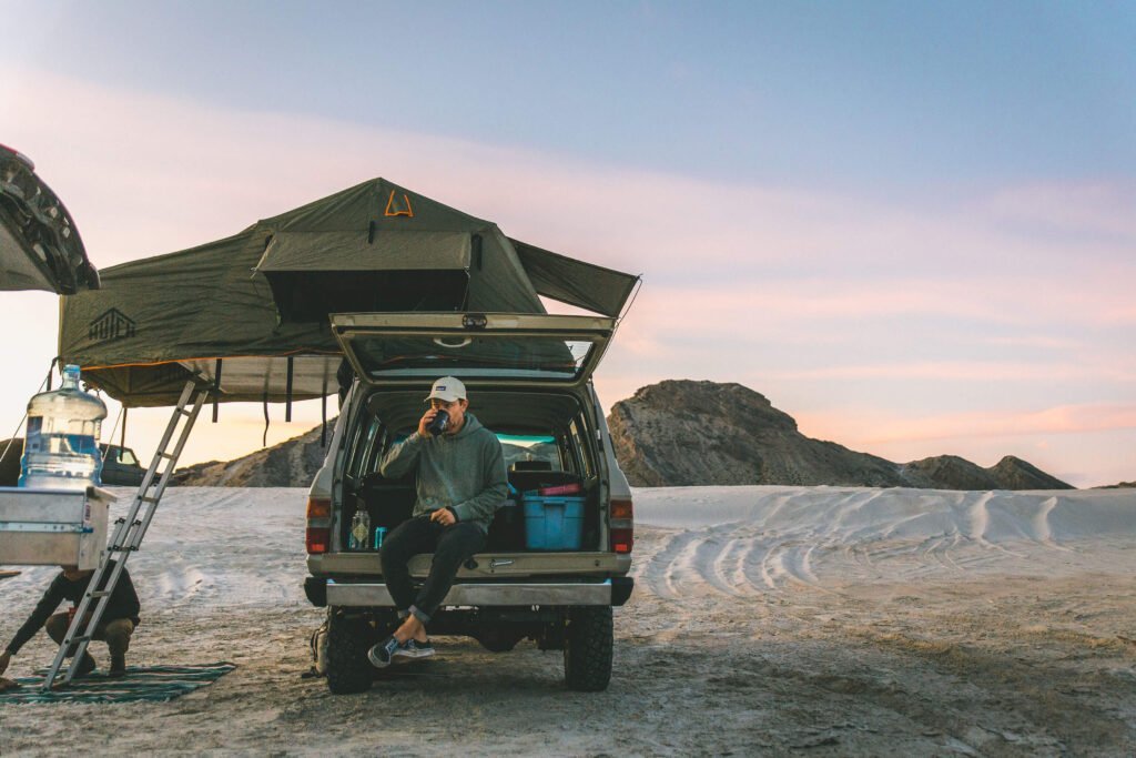 Land Cruiser with roof top tent and man drinking from cup.