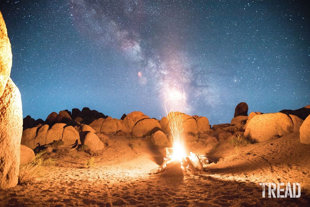 Campfire against large rocks and star-filled night sky