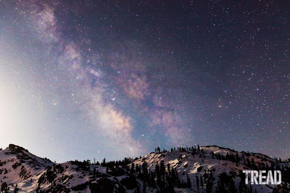 Snow and tree-filled mountainside with starry night sky