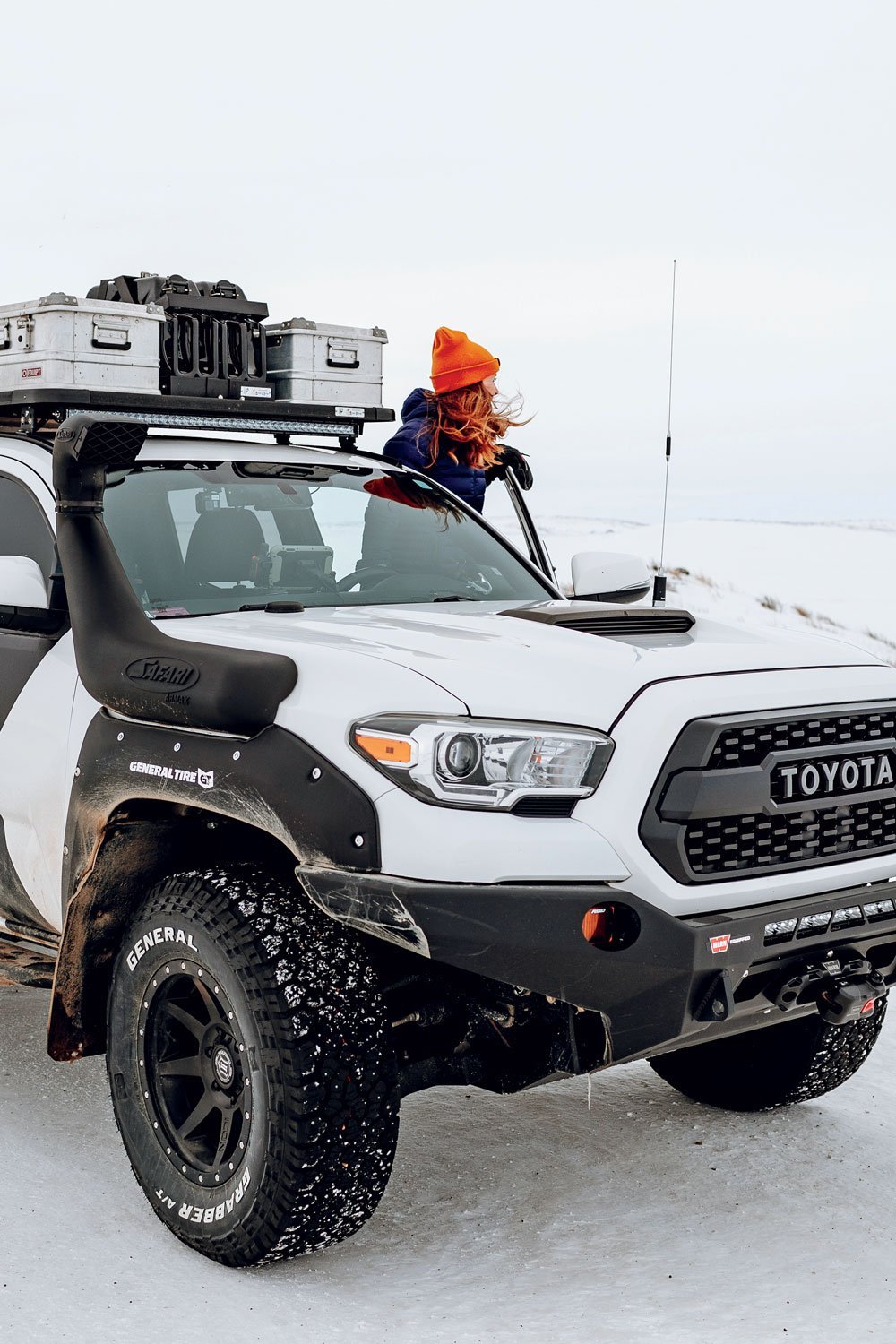 Woman looks off into the distance as she stands on Toyota Tacoma side step in snowy weather.