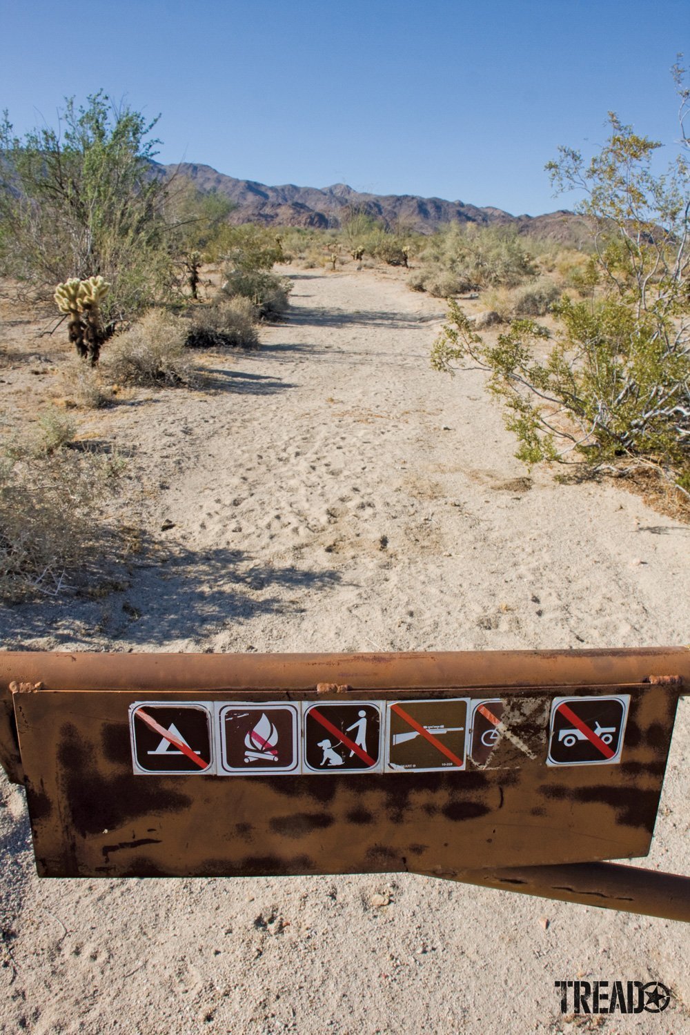 Desert dirt tail and rusted closed gate with no trespassing markers showing no entrance