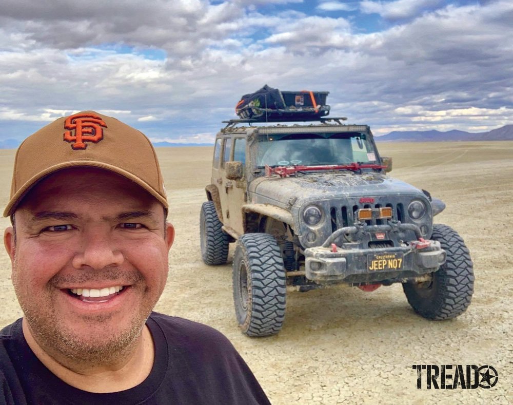 Roger Salazar stands near Jeep on dry lake bed.