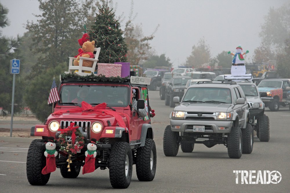 Various 4x4s are driving down the street, decorated with Christmas trees and presents, during a holiday parade