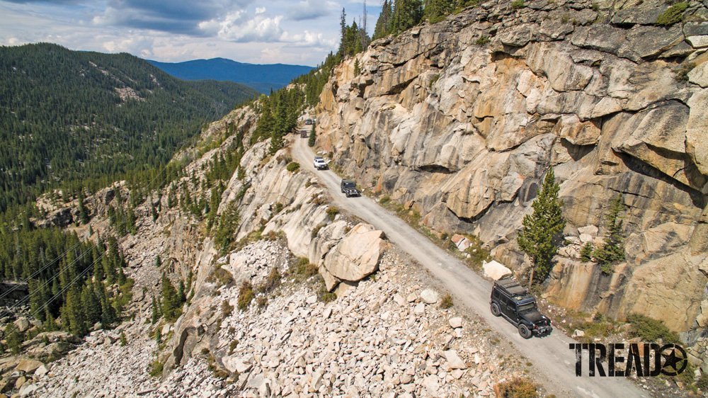 4x4s carefuly driving on cliffside trail in the middle of the mountains, with tan boulders and dirt