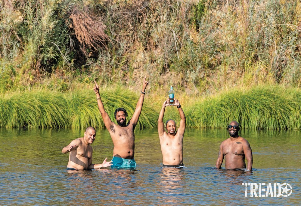 Camp Yoshi campers, in swim trunks, smile as they stand in a body of water. 