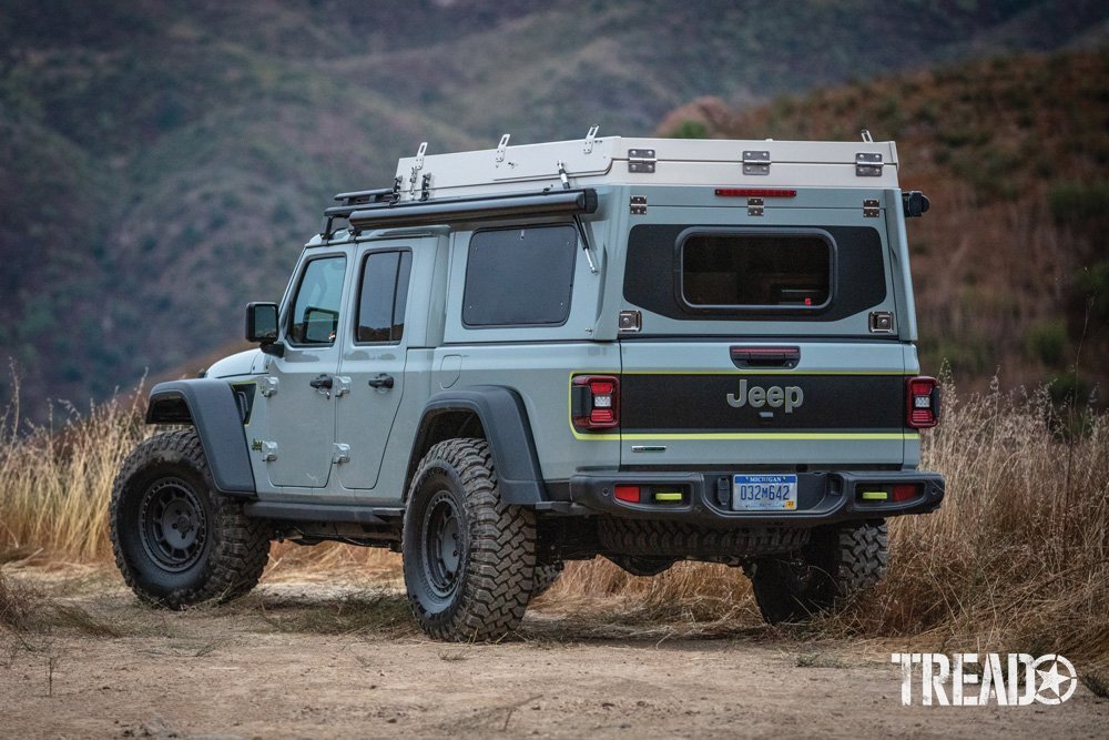 The Gladiator Farout has black wheels, knobby off-road tires, multicolored body and truck topper, with rooftop tent on its roof.