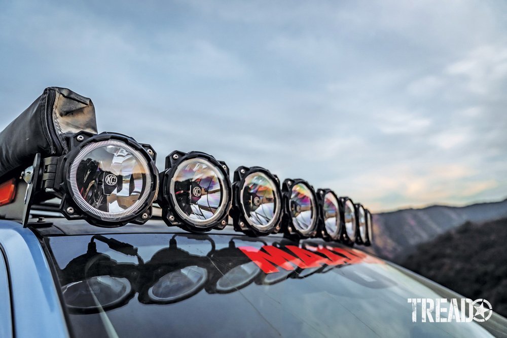 An array of KC HiLiTES aux driving lights are mounted on the 2019 Ford Ranger's roof rack, next to an awning.