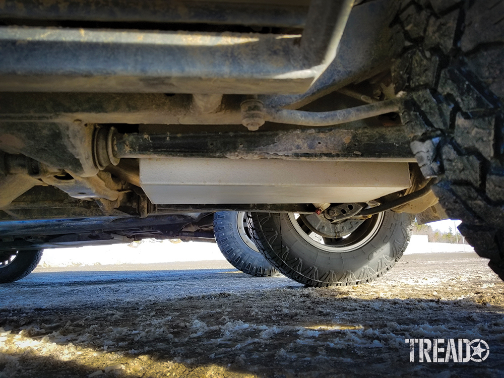 The Mitsubishi Pajero's silver auxiliary tank installed and showing in the vehicle's underbody as it sits on snowy ground.