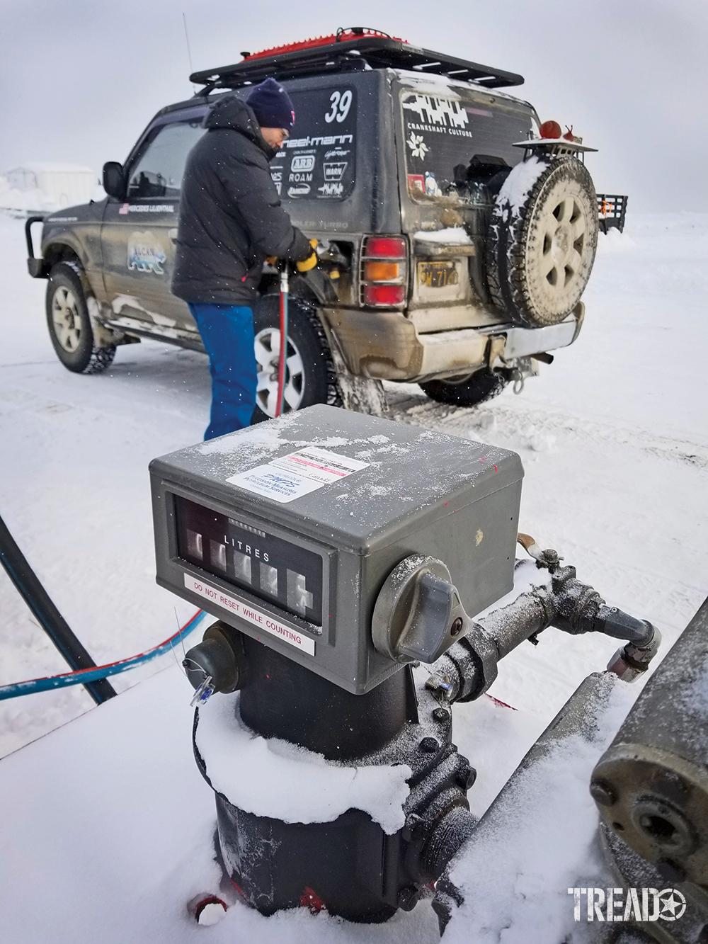 Andy Lilienthal, earing blue snow pants and black jacket fills up the dark gray Mitsubishi Pajero fuel tank and aux tank during the 2020 Alcan Rally. 