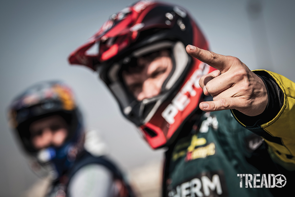 Outfitted with a helmet and black and yellow race suit, 2021 Dakar Simon Marcic of Team #46 in Jeddah motions with his hand.