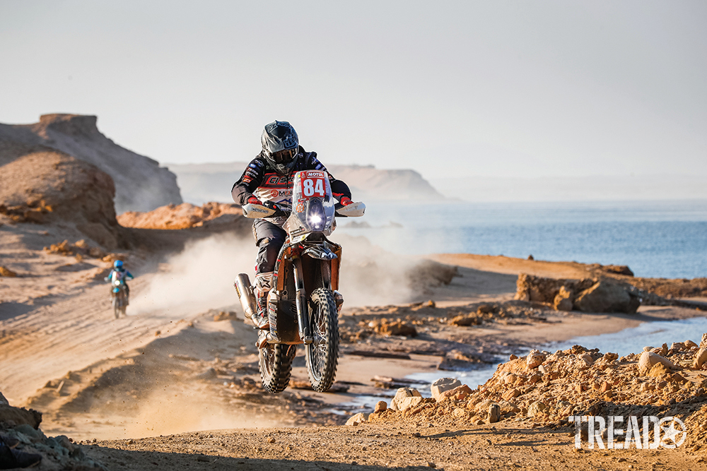 Two motocycler ralliers, 84 Hawker Neil (gbr), Husqvarna, Neil Hawker, drive quickly through dirt trails next to a body of water