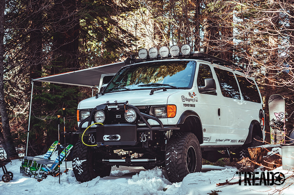 This Ford E350 Super Duty van is sitting in snow with awning set up. 