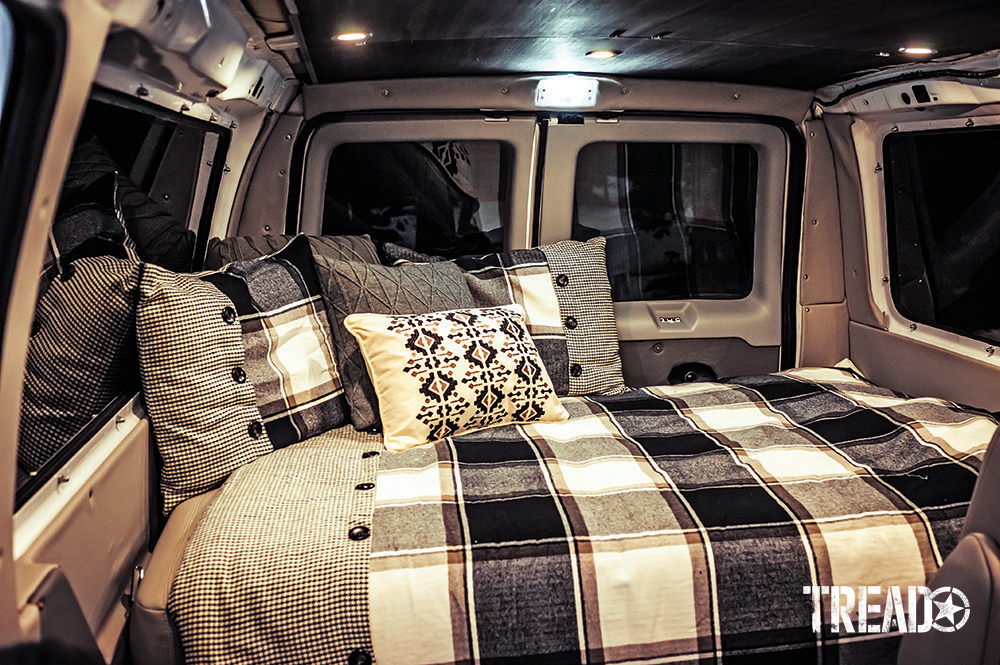 2006 Ford E350 Super Duty 4x4 sleeping area includes several pillows and a black and white oversized checkerboard blanket with buttons.