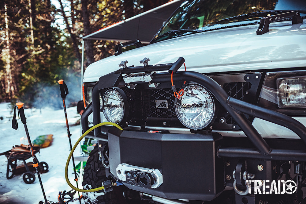 The white 2006 E350 Super Duty 4x4 has front upgrades like a beefy front bumper with bull bar, large auxiliary lights, and shovel.