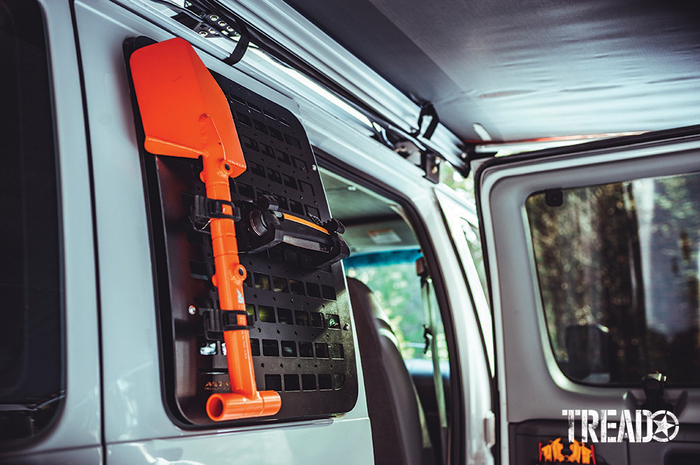 Agency 6 black GRIDS MOLLE and orange shovel is mounted on a read white van door.