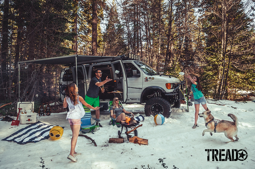 The Montes family are playing catch next to their 2006 Ford E350 Super Duty 4x4 while at camp in the woods.