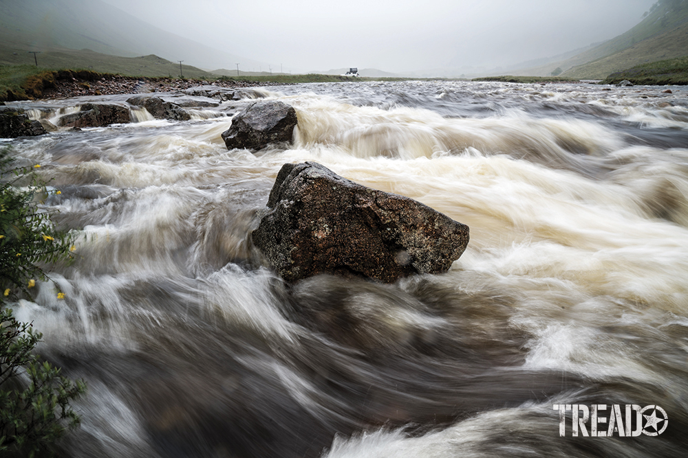 Scotland's quick-moving waterway show whitewater zipping through large boulders in front of gray skies.