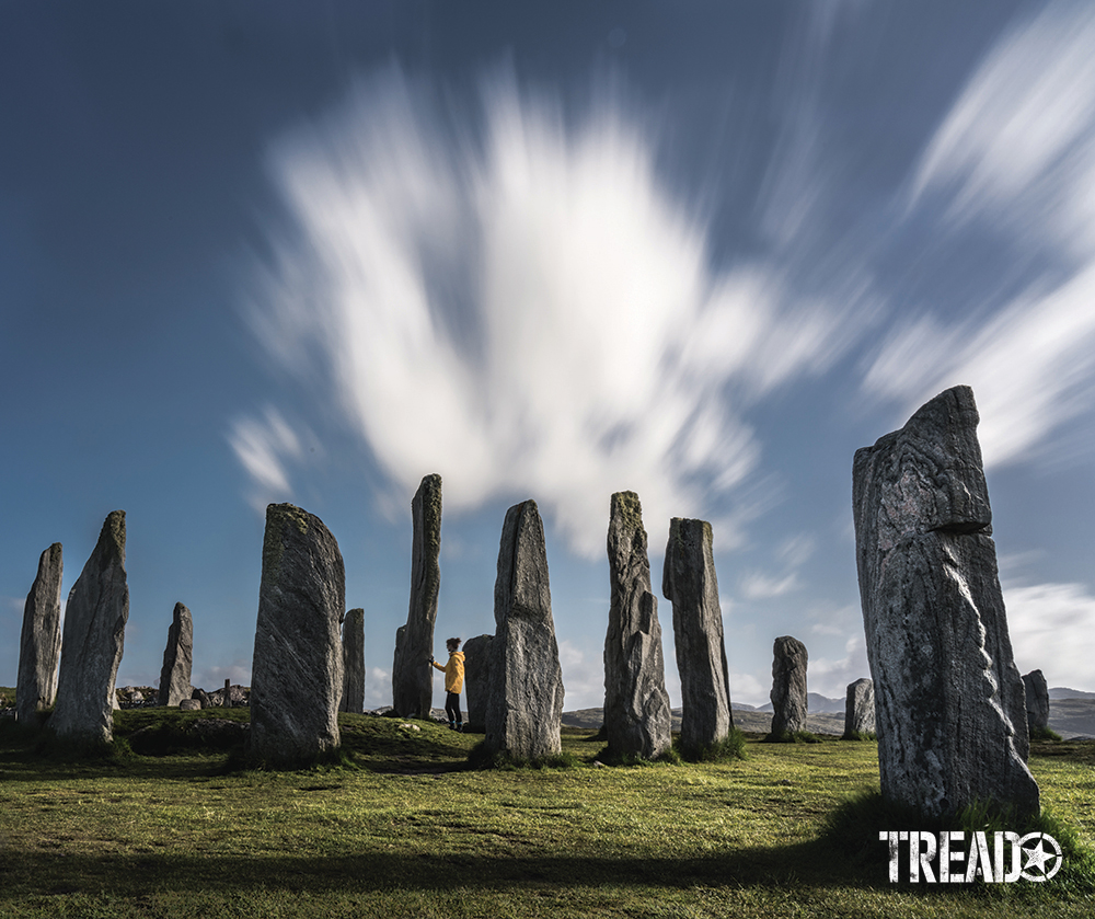 The Callanish Standing Stones loom over short green grasses while some clouds wisp away overhead. 