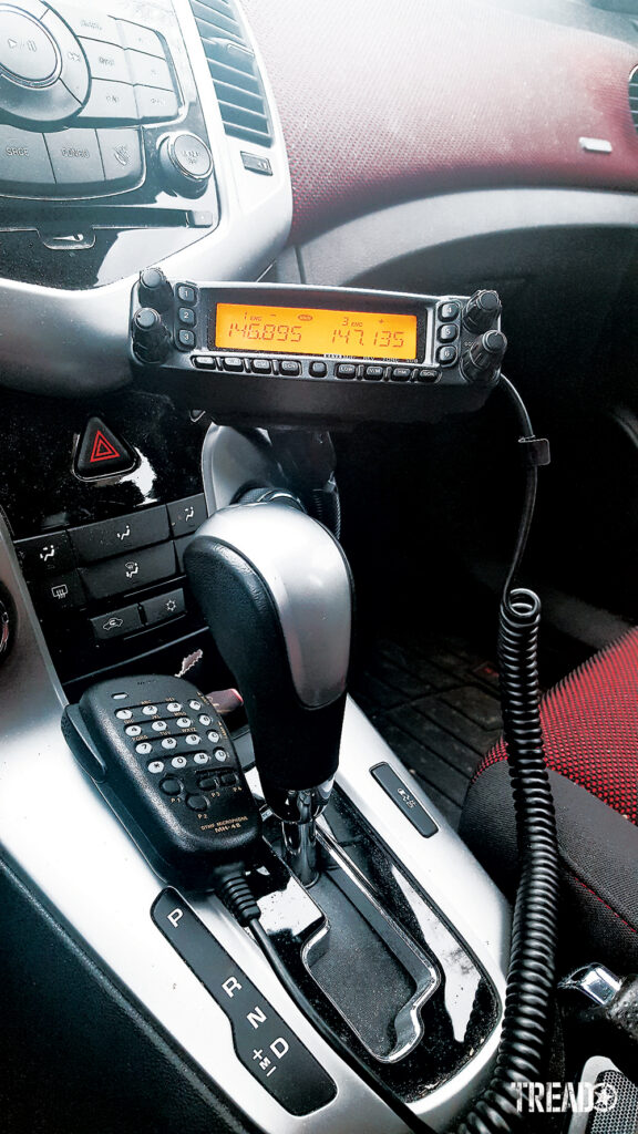 A hardwired radio is mounted near the center of a vehicle with a silver, gray, and red interior.