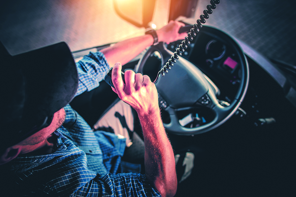 A man grabs the mounted radio's receiver with his right hand while driving.