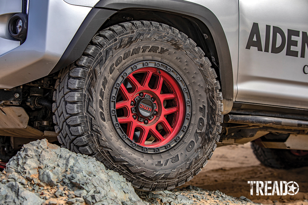 17-inch KMC candy red wheels and beefy Toyo Tires Open Country off-road tires sit on two large rocks.