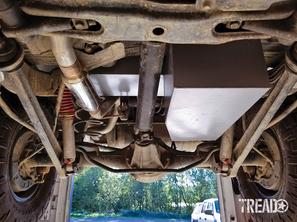 An LRA auxiliary fuel tank is nestled in the Pajero's underbody, next to white and red shocks and knobby tires. 