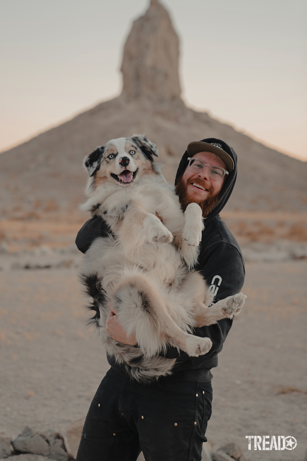 Kingston holds his dog Shadow, with a pointed rock formation behind them. 