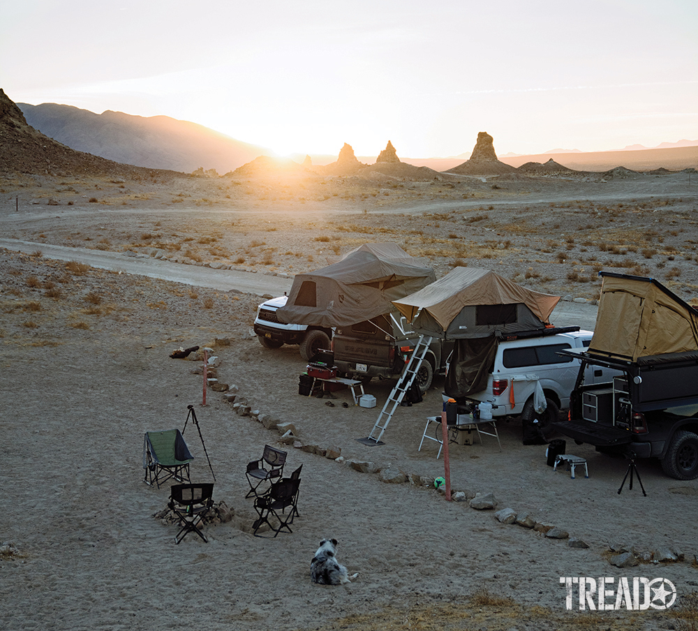 Four adventure vehicles are parked in a desert remote camp area, waiting for the sun to go down. 