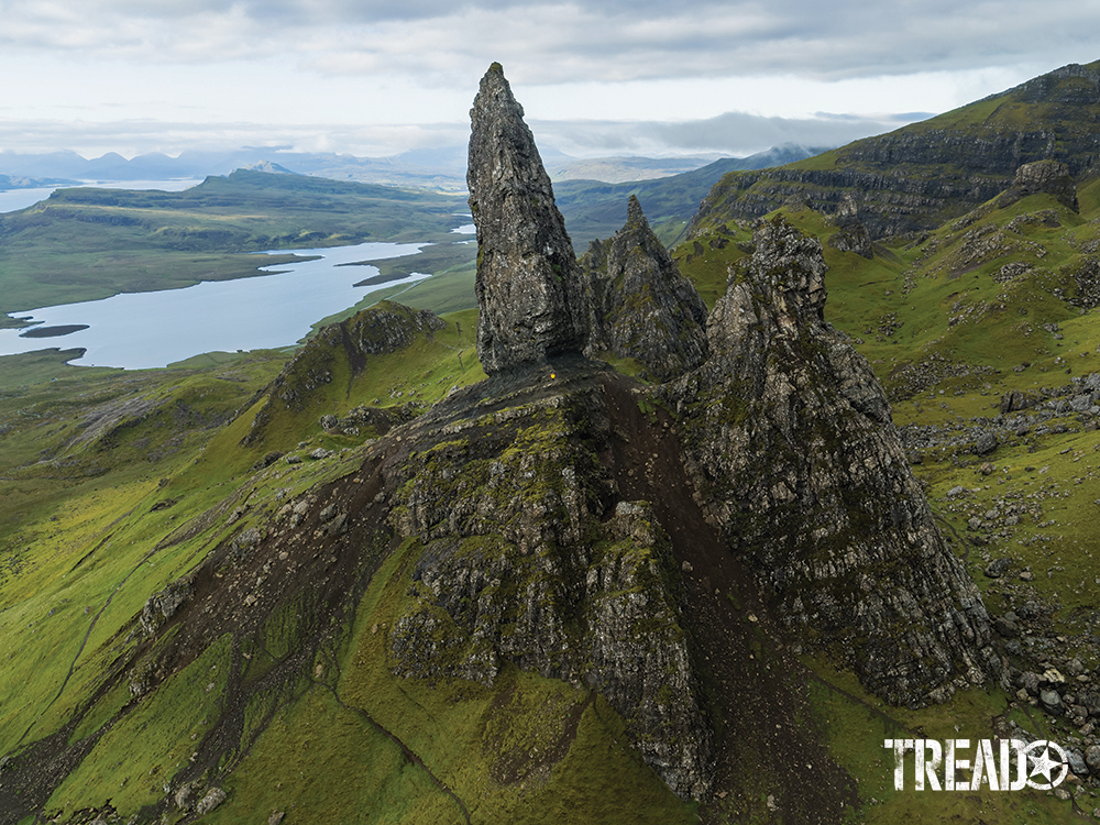 The Old Man of Storr rock formation soars over lush, green Scottish countryside and waterways.