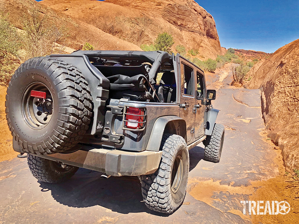 A customized gray Jeep with Titan spare tire tank is driving over Moab's Hell's Revenge Trail.