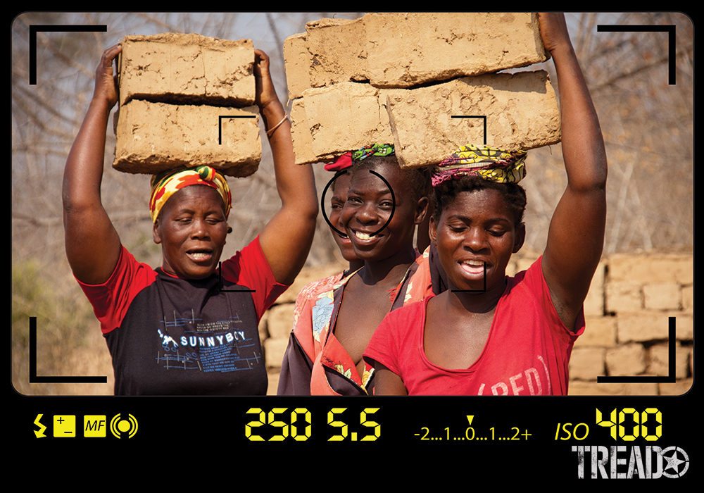 The ladies of a small village, near Lake Kariba, Zambia, have dark skin and wear brightly colored clothing as they carry mud bricks on their head.