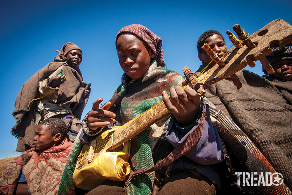 Dark-skinned children playing water can drums and guitars crafted from scrap lumber and corn oil jugs.