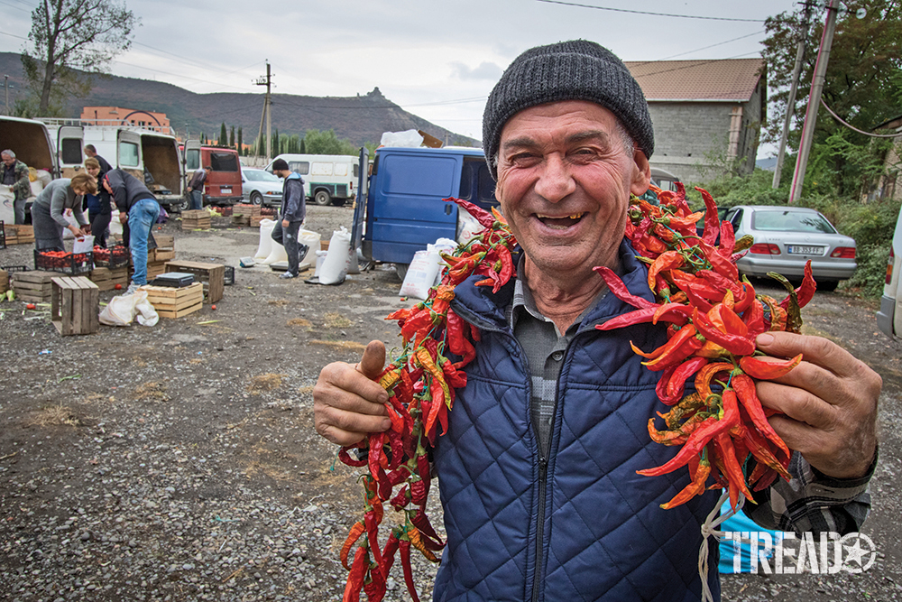 Soviet Republic of Georgia smiling food vendor with gray hat, blue quilted jacket, and peppers around his neck.