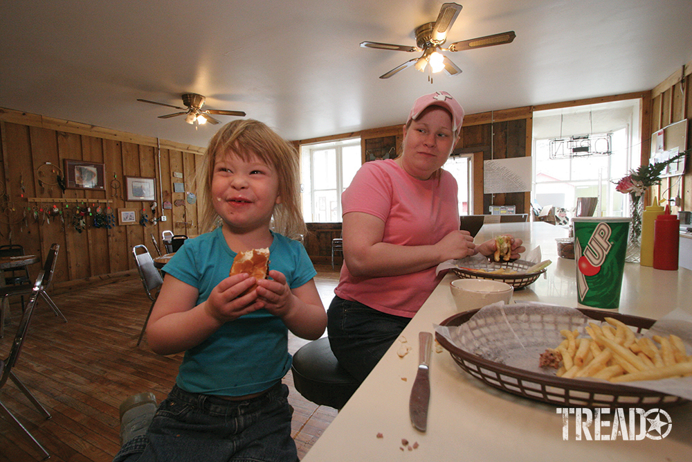 The café in Lone, with proprietor and daughter, eating french fries sitting on stools in wood-paneled interior with ceiling fans.