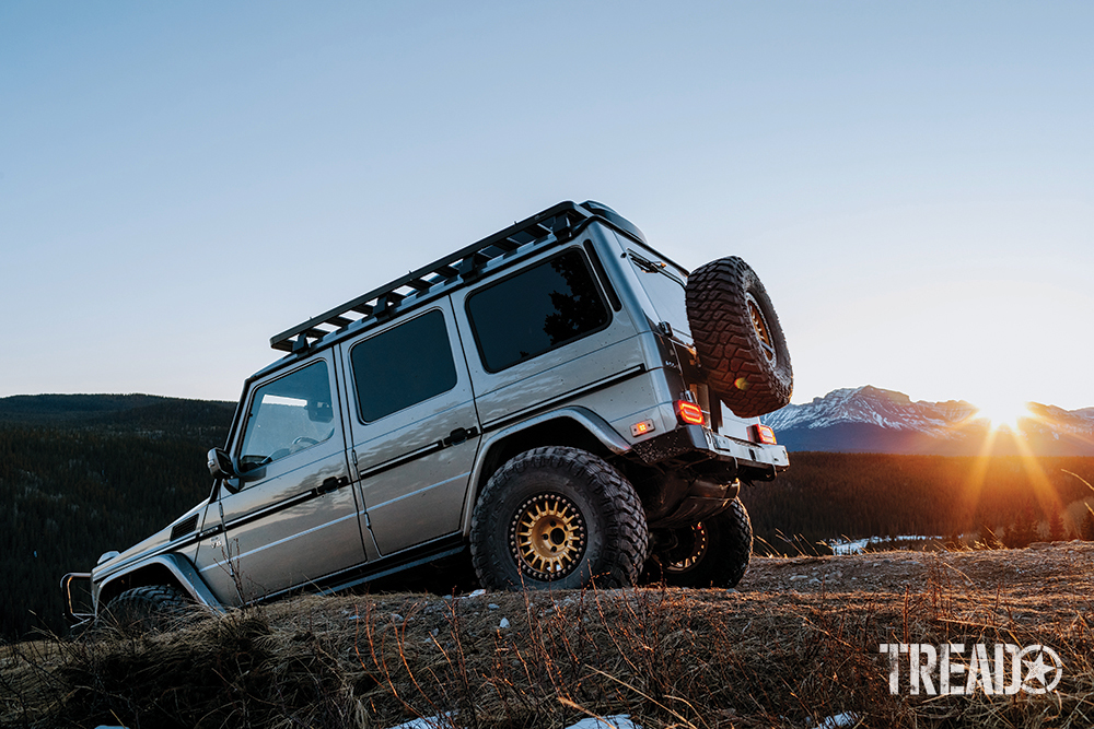 The silver 2004 Mercedes AMG G55 G-Wagen goes downhill during sunset.