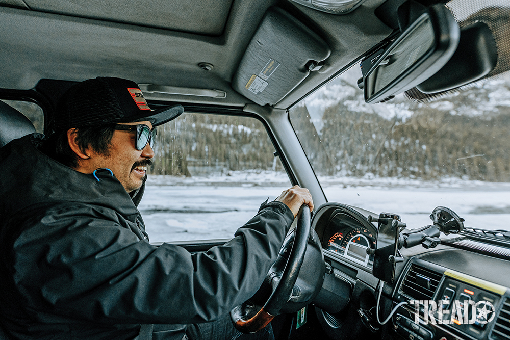 Nathan, wearing gray jacket and black hat with mustache, smiles as he drives his Mercedes G-Wagen.