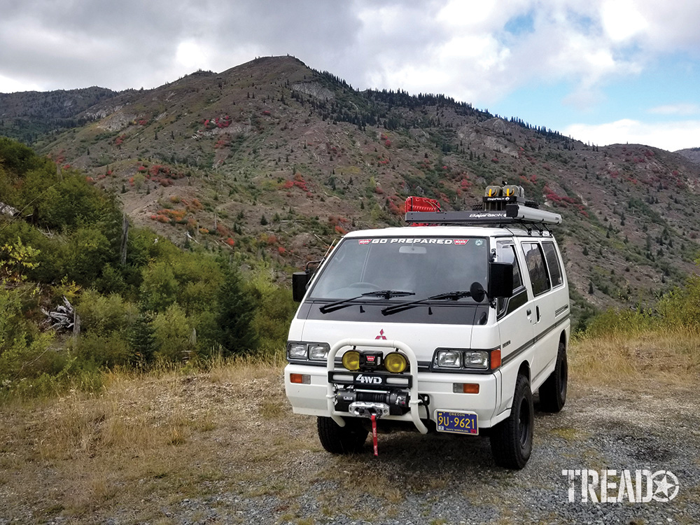 A white Mitsubishi Delica Star Wagon is parked on a grassy hillside.