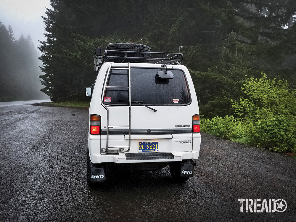 The rear view of the Mistubishi Delica L300 with a roof rack and ladder mounted to the rear hatch door.