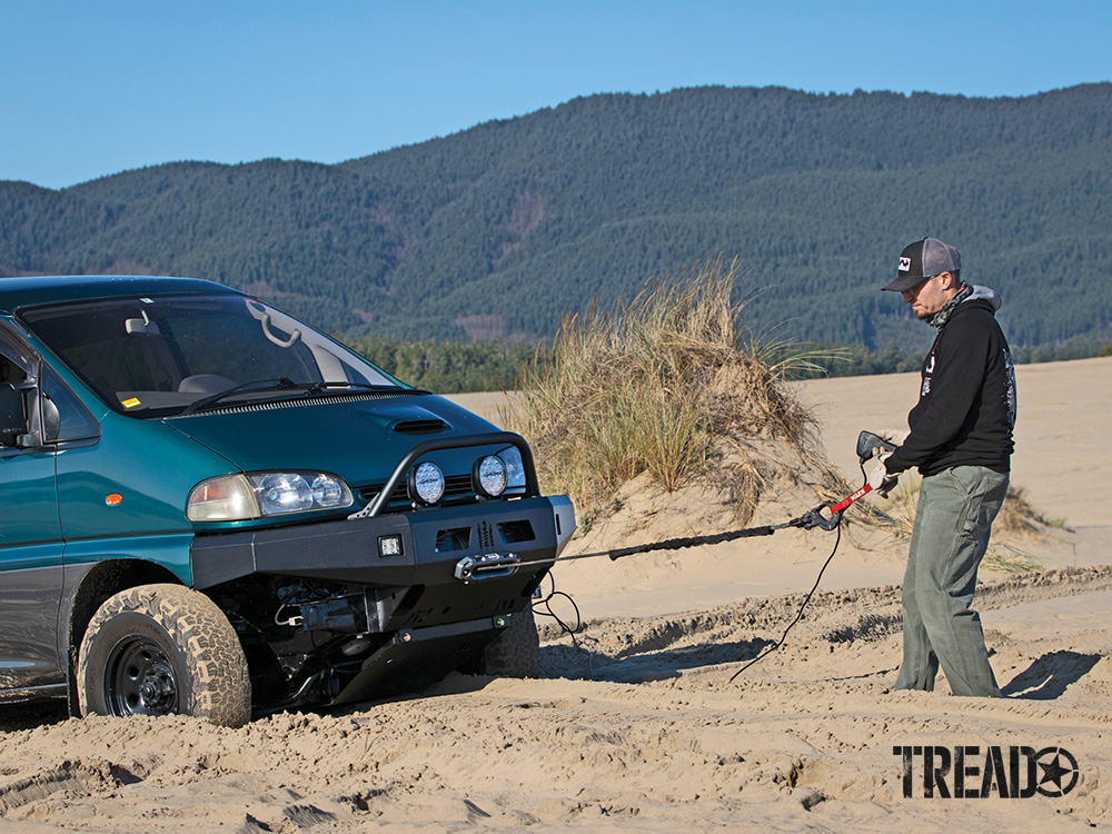 A land anchor is coupled with a winch to help pull a green Mitsubishi Delica van that is stuck in the sand dunes.