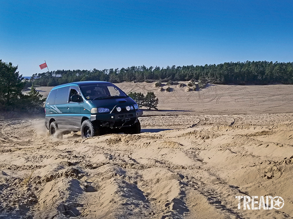 A green Mitsubishi Delica Space Gear L400 takes quick turns in the sand.