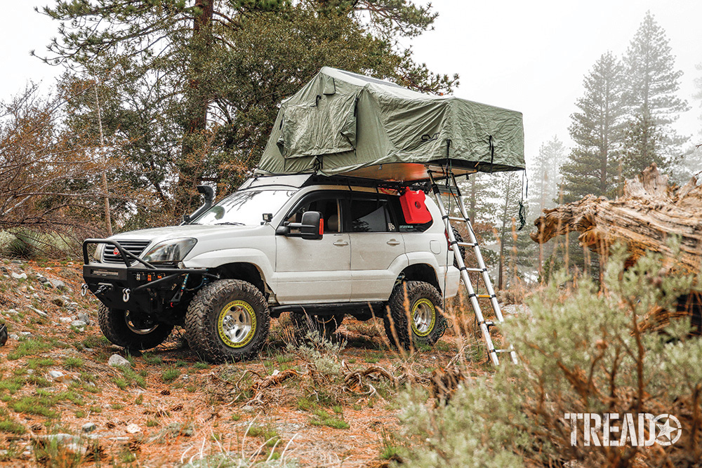 A white Off-road Lexus GX 470 has sage colored rooftop tent open with ladder deployed.