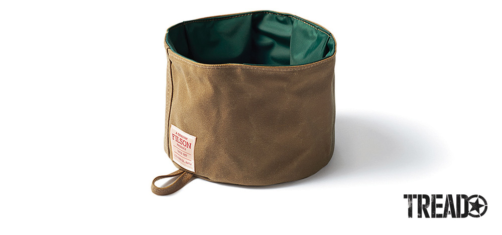 The collapsible tan and green dog bowl from Filson folds to store in a pocket or clips onto your pack with the attached hanging loop.